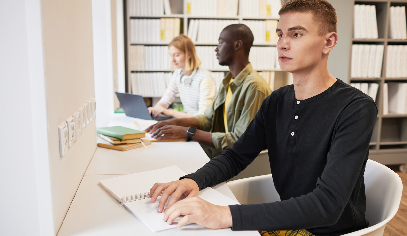 Group of students with young man reading braille book in library